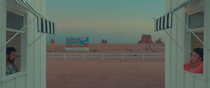 Asteroid City characters looking from their hotel bungalows, the desert landscape, with a sign for a casino, between them.